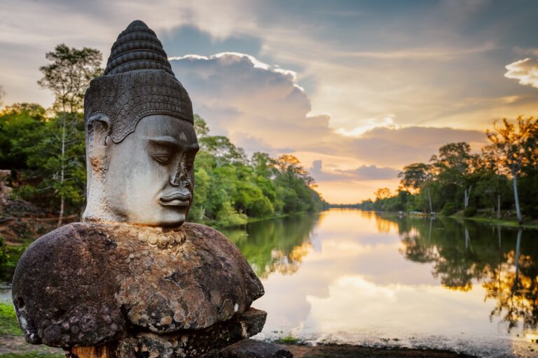 Stone Asura and sunset over moat surrounding Angkor in Cambodia