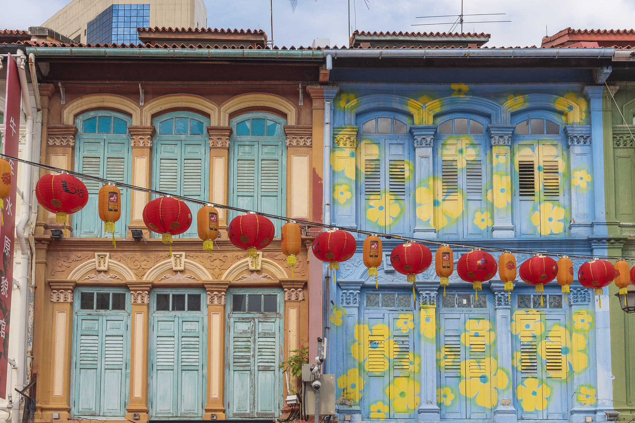 An image of a row of colorful shophouses in pastel tones, with red lanterns hanging across the street in front. The shophouses feature arches, shutters, and ornate architectural details. Consider exploring these vibrant sights with tour packages with airfare from the USA now available.