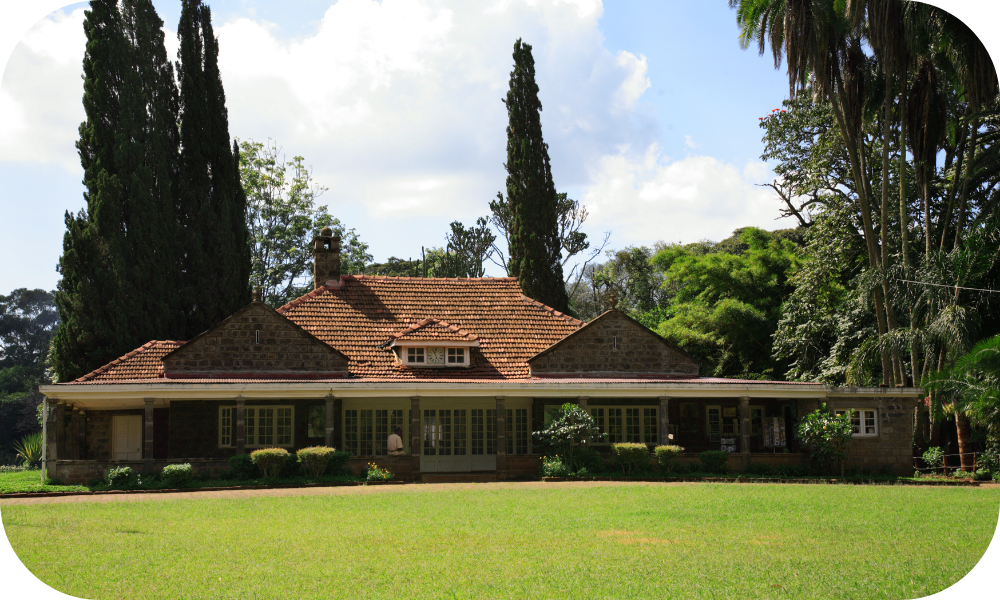 A charming stone house with a tiled roof, surrounded by lush greenery and tall trees under a partly cloudy sky. The lawn in front is well-maintained, adding to the serene setting, offering incredible deals for those seeking tranquility and beauty.