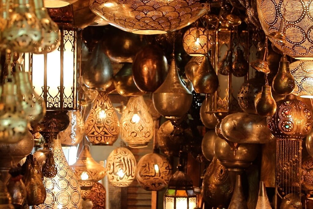 A captivating assortment of intricately designed hanging lanterns and lamps in various shapes, sizes, and patterns, illuminated with warm, soft lighting. The metallic textures and ornate details create a rich, golden-hued ambiance reminiscent of the exotic charm you'd find in top Egypt tour packages.